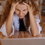 Frau mit gestresstem Gesichtsausdruck am Laptop, symbolisiert den Umgang mit Stress und die Wichtigkeit von Selbstmitgefühl.
