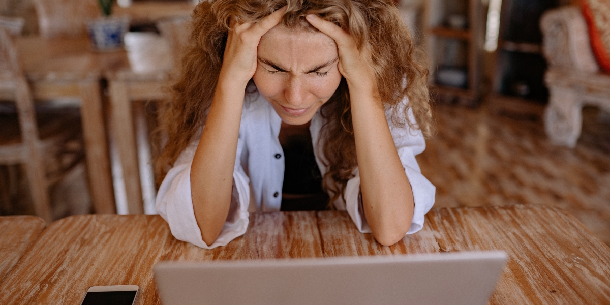 Frau mit gestresstem Gesichtsausdruck am Laptop, symbolisiert den Umgang mit Stress und die Wichtigkeit von Selbstmitgefühl.